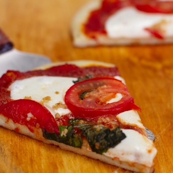A slice of Margherita pizza with fresh tomatoes, mozzarella, and basil on a wooden board.