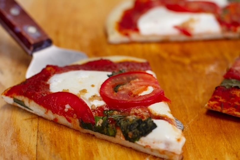 A slice of Margherita pizza with fresh tomatoes, mozzarella, and basil on a wooden board.