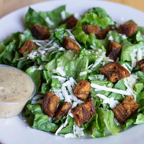 Caesar salad with green lettuce, shredded cheese, croutons, and a side of dressing.