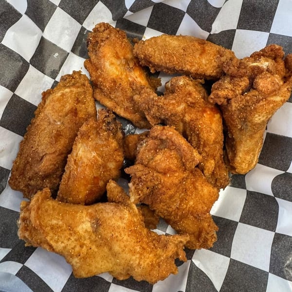 Crispy fried chicken wings seasoned with spices, served on black and white checkered paper.