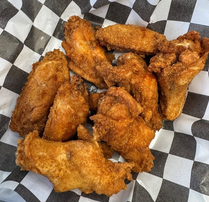 Crispy fried chicken wings seasoned with spices, served on black and white checkered paper.
