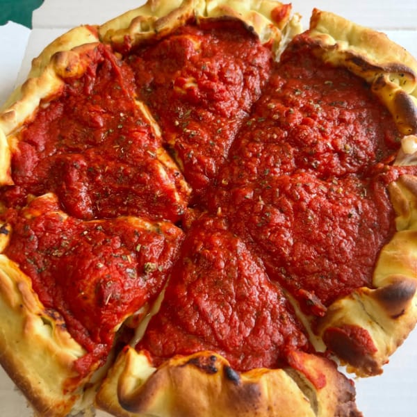 Deep dish pizza with thick red sauce and golden crust, sliced into six pieces in a white box.