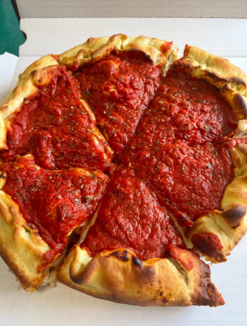 Deep dish pizza with thick red sauce and golden crust, sliced into six pieces in a white box.