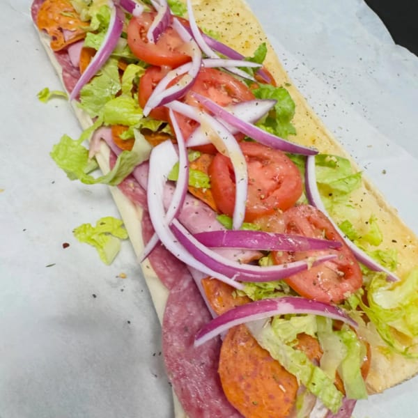 A large deli sub sandwich with salami, pepperoni, lettuce, tomatoes, and red onions.