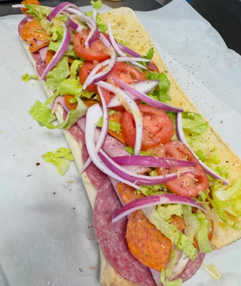 A large deli sub sandwich with salami, pepperoni, lettuce, tomatoes, and red onions.
