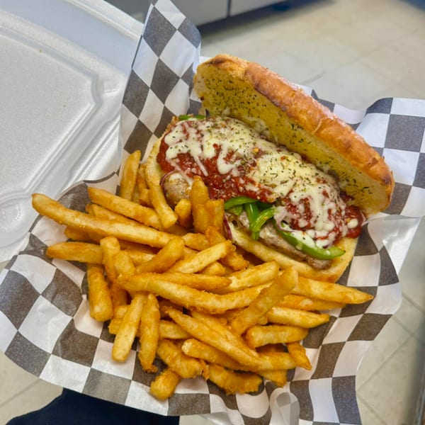Sausage and pepper sub with melted cheese and marinara, served with a side of french fries.