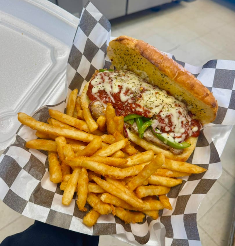 Sausage and pepper sub with melted cheese and marinara, served with a side of french fries.