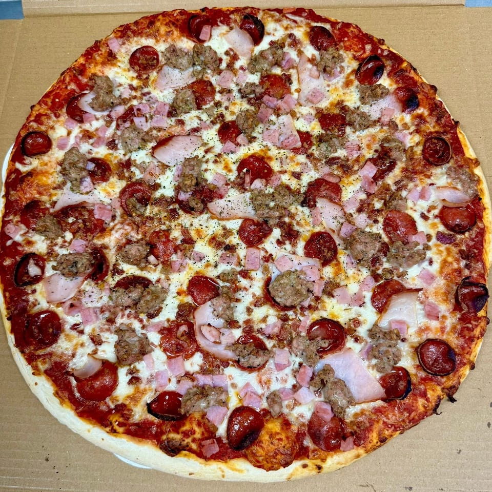 A whole meat lover's pizza with pepperoni, sausage, ham, and bacon in a cardboard box.