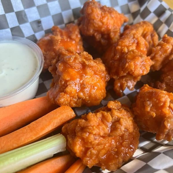 Buffalo chicken bites with ranch dressing, carrots, and celery in a checkered paper-lined basket.