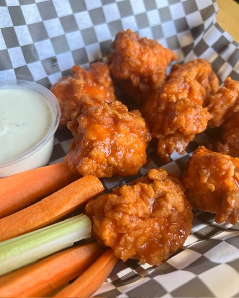 Buffalo chicken bites with ranch dressing, carrots, and celery in a checkered paper-lined basket.